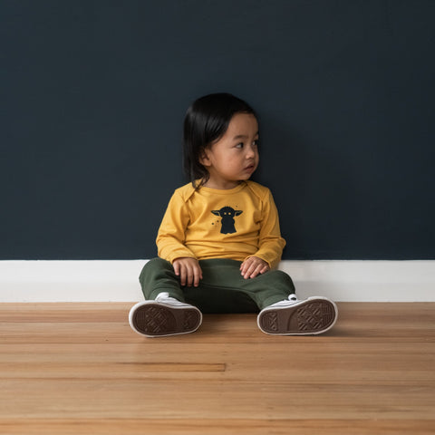 Child wearing trackies and merino baby long sleeve top canary yellow with print