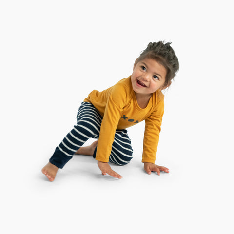 Child wearing slouch pants and merino baby long sleeve top nugget yellow with print